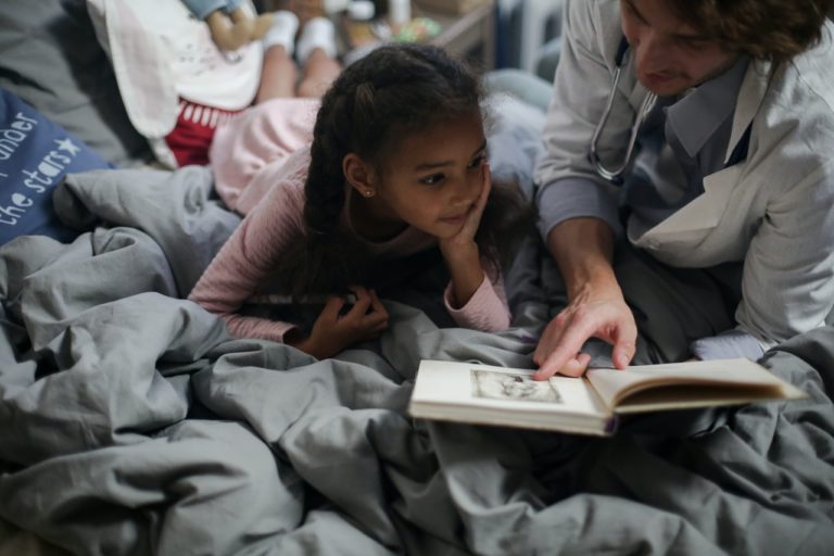 Child lying on a bed, reading a book with a dentist
