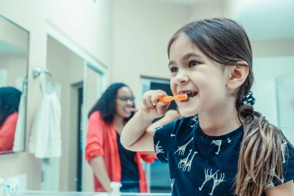 A kid brushing her teeth with her mother
