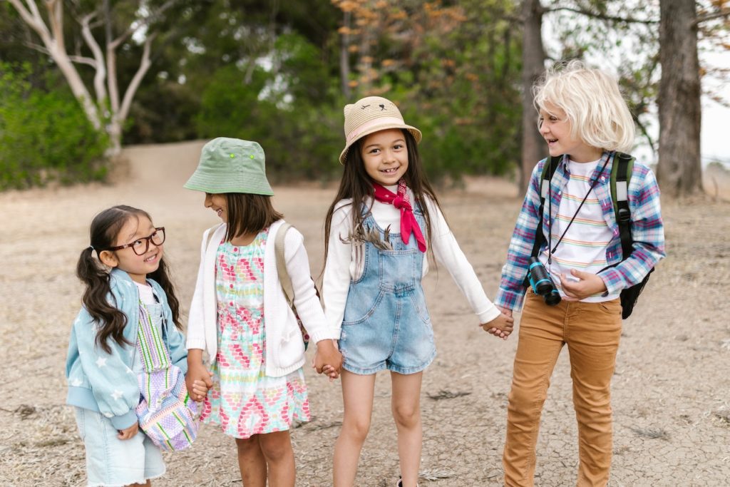 Four children holding hands and smiling while on a hike